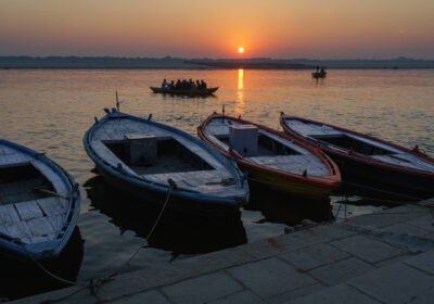 Wooden rowboats moored at a Varanasi ghat at sunrise with the Ganges glowing gold