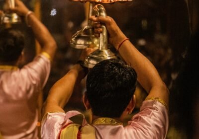 Priest raising a multi-tiered brass lamp during the Ganga Aarti fire ritual, flames lit against the night
